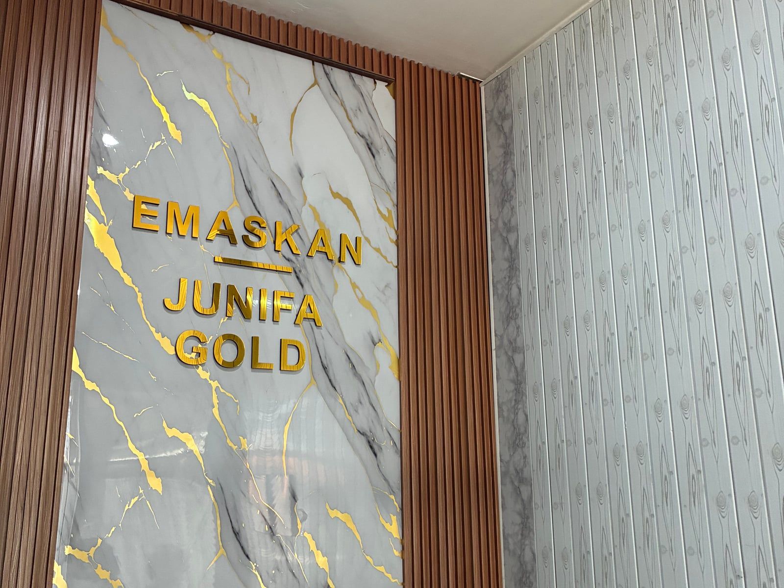 Papan nama EMASKAN dan Junifa Gold berhuruf emas di dinding marmer toko Junifa Gold, Denpasar